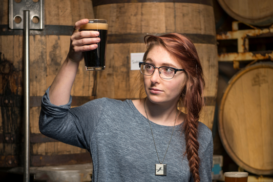 Woman testing a dark beer in the barrel room
